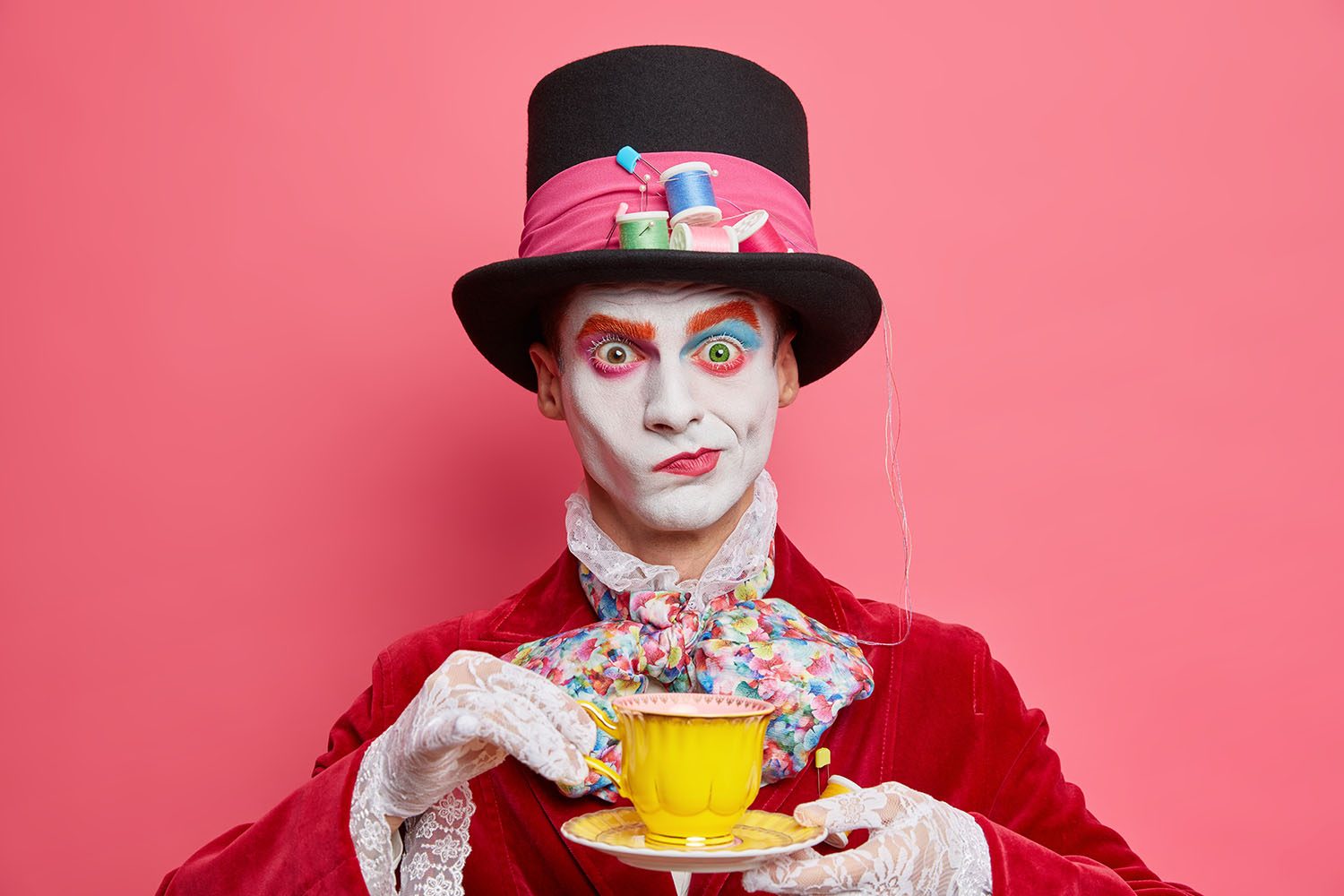 Horizontal shot of serious male hatter poses with cup of tea wears hat has manners of aristocratic gentleman dresses for masquerade carnival poses indoor. Halloween and entertainment concept